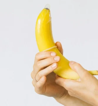 Mano colocando un condón en un plátano, representación de educación sexual y uso correcto del preservativo.