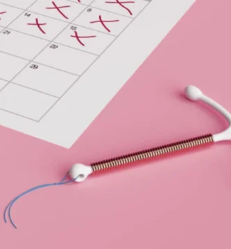 Dispositivo intrauterino (DIU) sobre fondo rosa junto a un calendario con fechas marcadas, representando el control anticonceptivo.