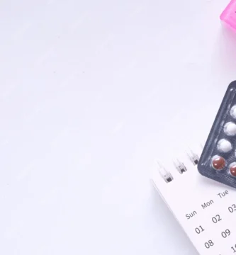 Blíster de pastillas anticonceptivas junto a un calendario menstrual y pastillero semanal